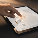 Gros plan d'une main qui touche l'écran d'une tablette affichant une interface web épurée, pour illustrer l'expérience utilisateur (UX).